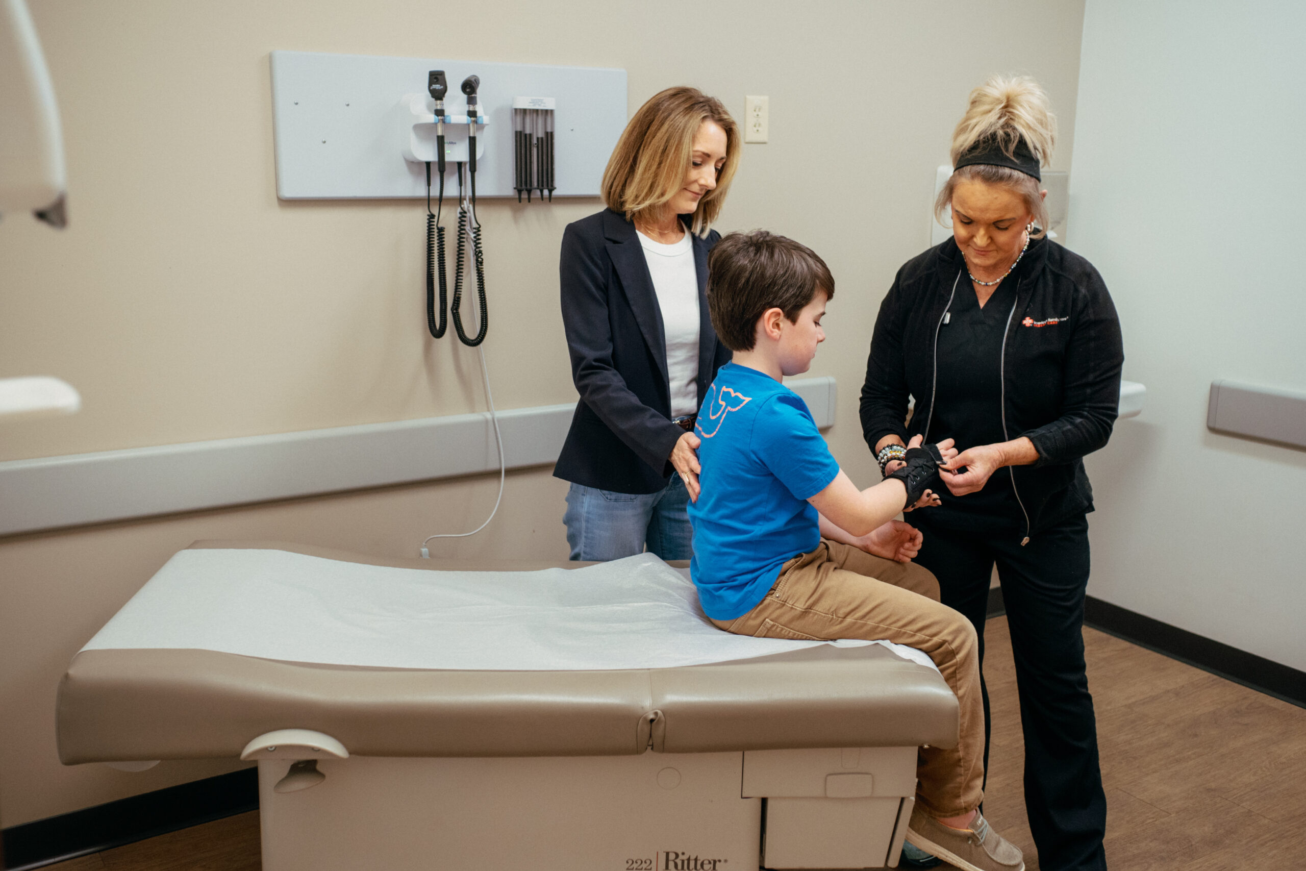 Pediatric healthcare professional examining and treating a young patient's wrist during a medical appointment.